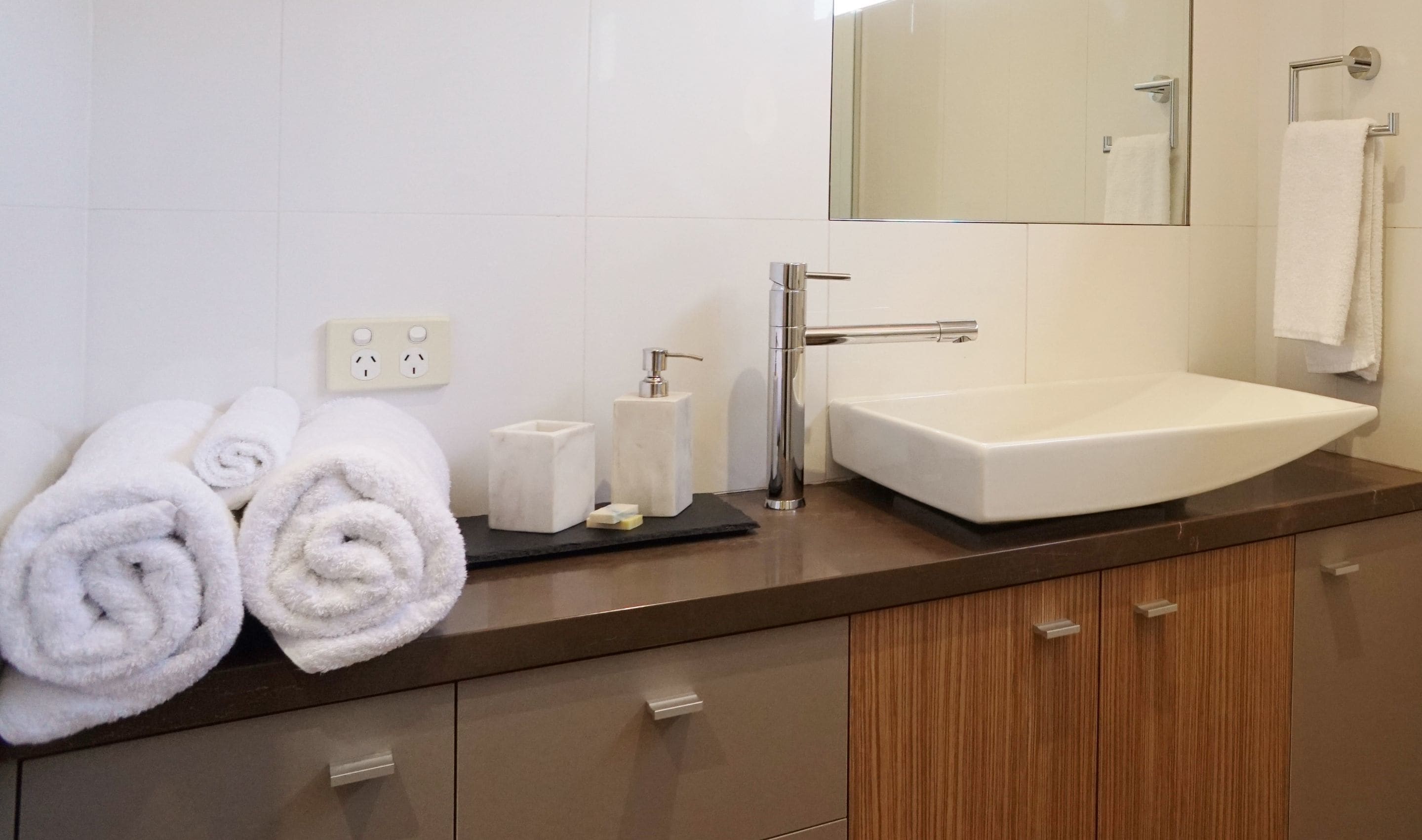 A bathroom with a white sink, a mirror, and two rolled towels on the counter.