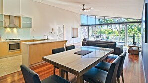Una cocina moderna con una isla central, comedor con mesa y sillas de madera, y un ventanal con vistas al exterior.