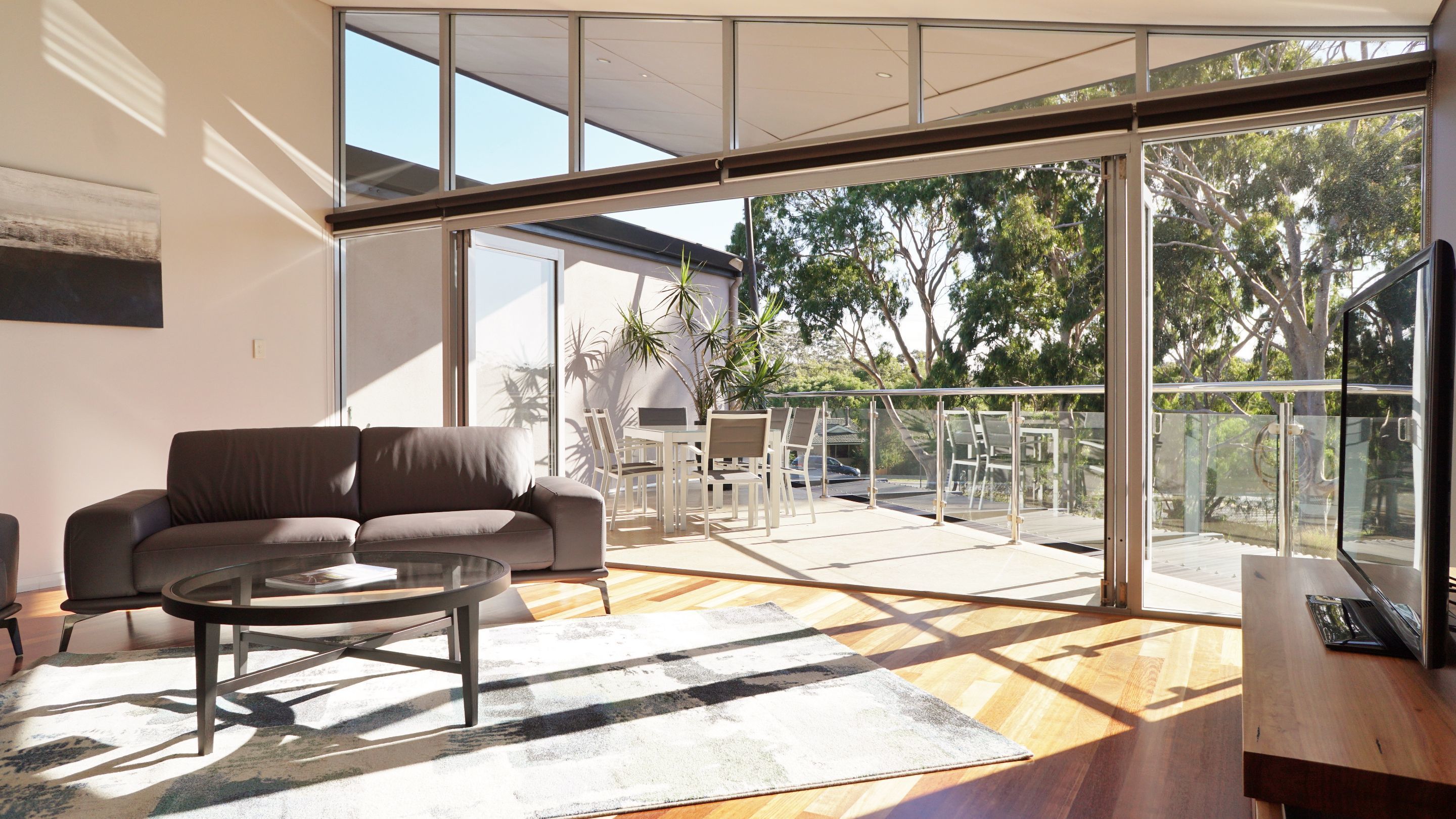 A modern living room with a sofa, coffee table, and a balcony with outdoor seating.