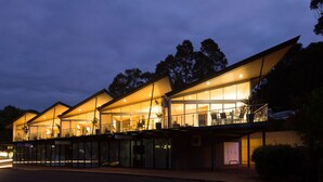 Un edificio moderno con grandes ventanales y techo plano, que cuenta con una zona de estar exterior cubierta y una entrada visible.