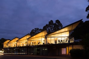 Un edificio moderno con grandes ventanales y techo plano, que cuenta con una zona de estar exterior cubierta y una entrada visible.