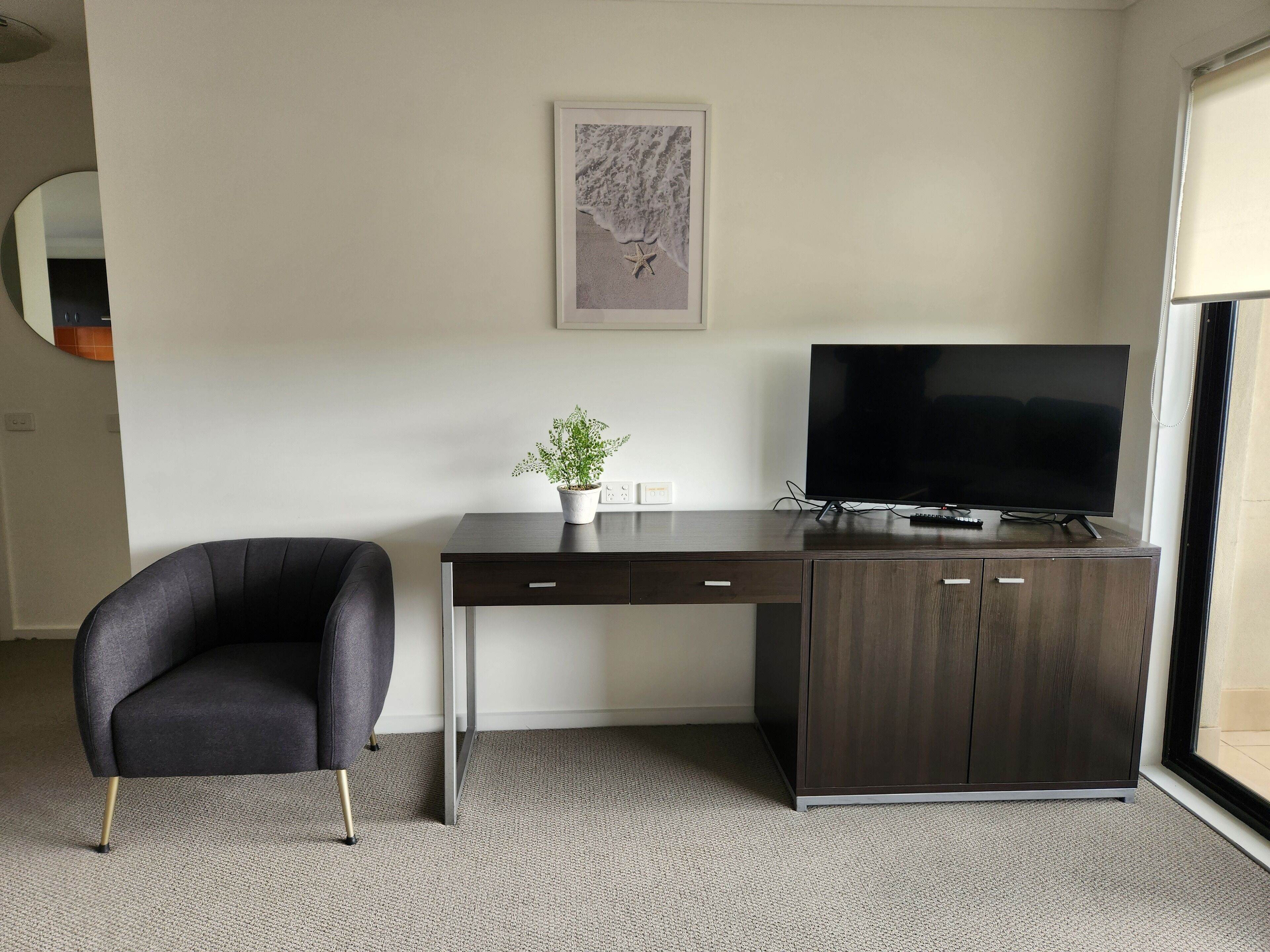 Een moderne kamer met een donker houten bureau, een zwarte stoel, een televisie en een kleine potplant.