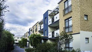 A row of modern multi-story residential buildings with balconies, a paved walkway, and surrounding greenery. - Oceanic On Thompson Apartments (Cowes)