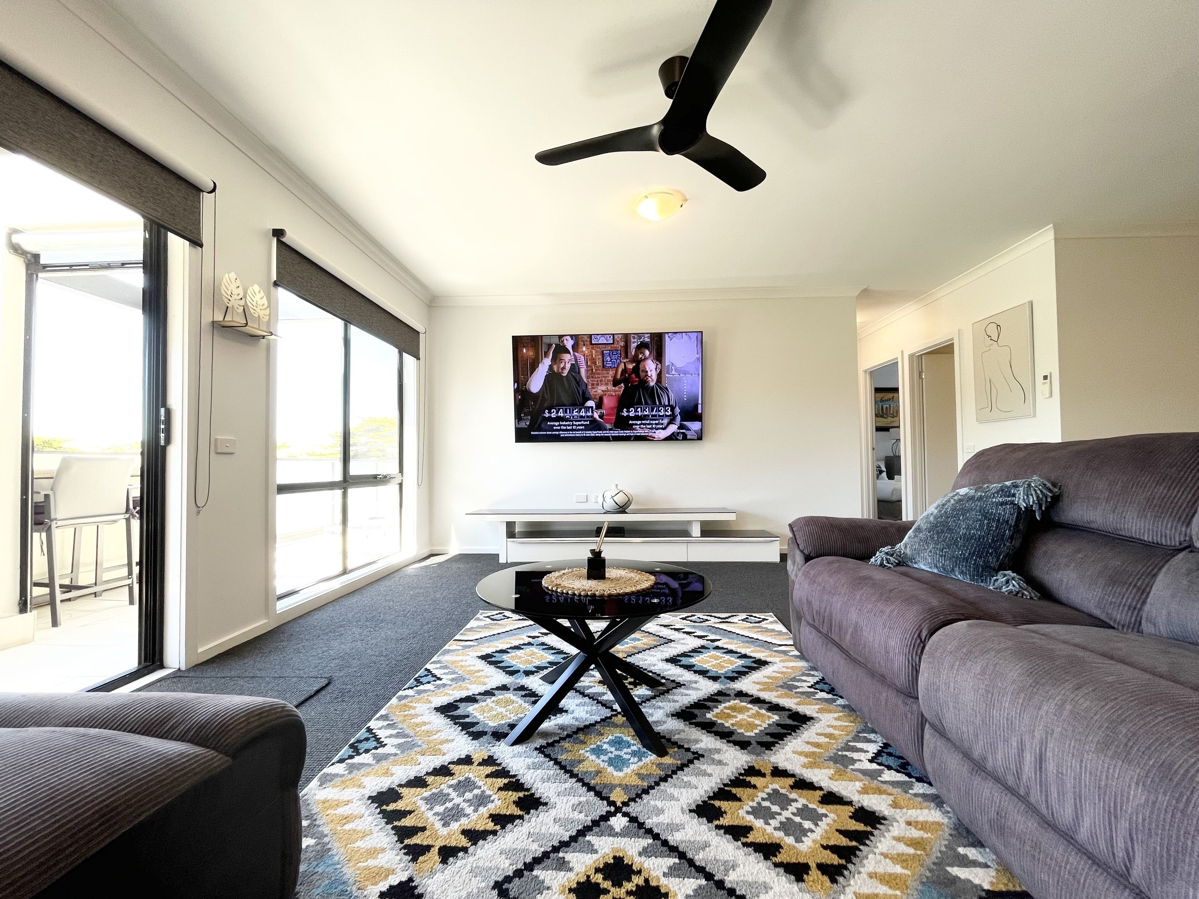 Una sala de estar moderna con un sofá gris, un tapete estampado, un televisor de pantalla plana y un ventilador de techo.