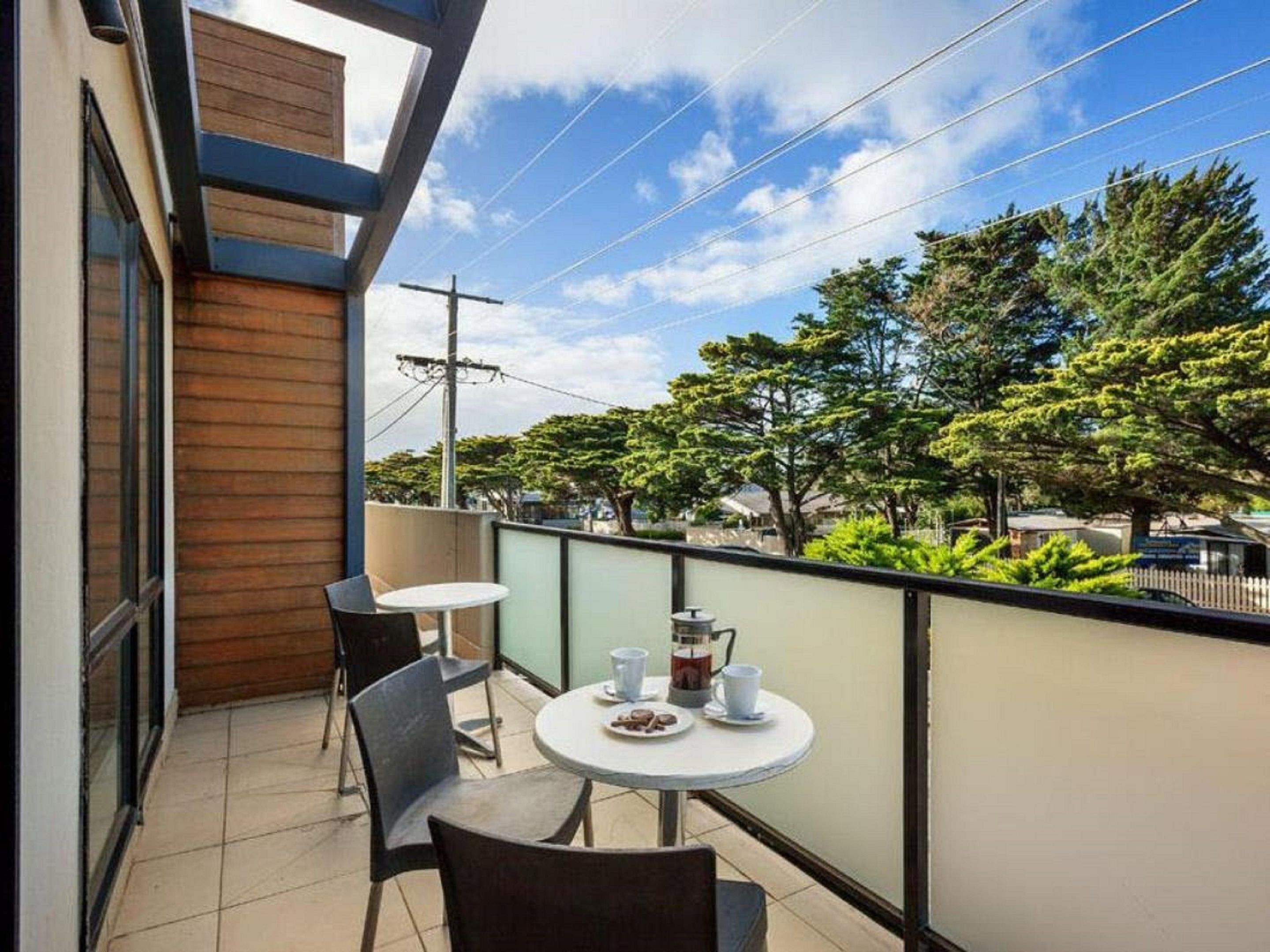 A balcony with a table and chairs, a coffee maker, and a view of trees and buildings.