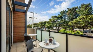 A balcony with a table and chairs, a coffee maker, and a view of trees and buildings.