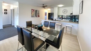 A modern kitchen with a refrigerator, microwave, and sink. There is a dining area with a glass table and chairs. - Oceanic On Thompson Apartments (Cowes)