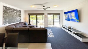 A modern living room with a sectional sofa, a flat-screen TV, and a cityscape painting. - Oceanic On Thompson Apartments (Cowes)