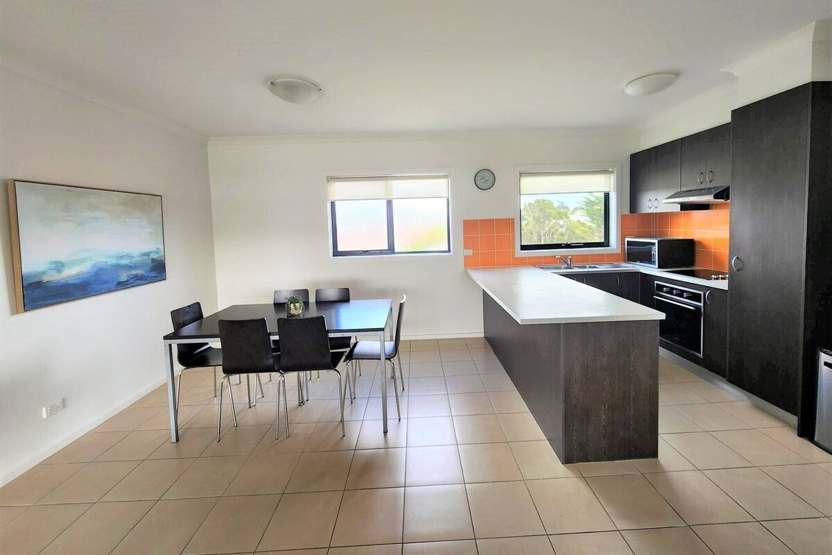 A modern kitchen with a central island, a dining area with chairs, and a large window providing natural light.