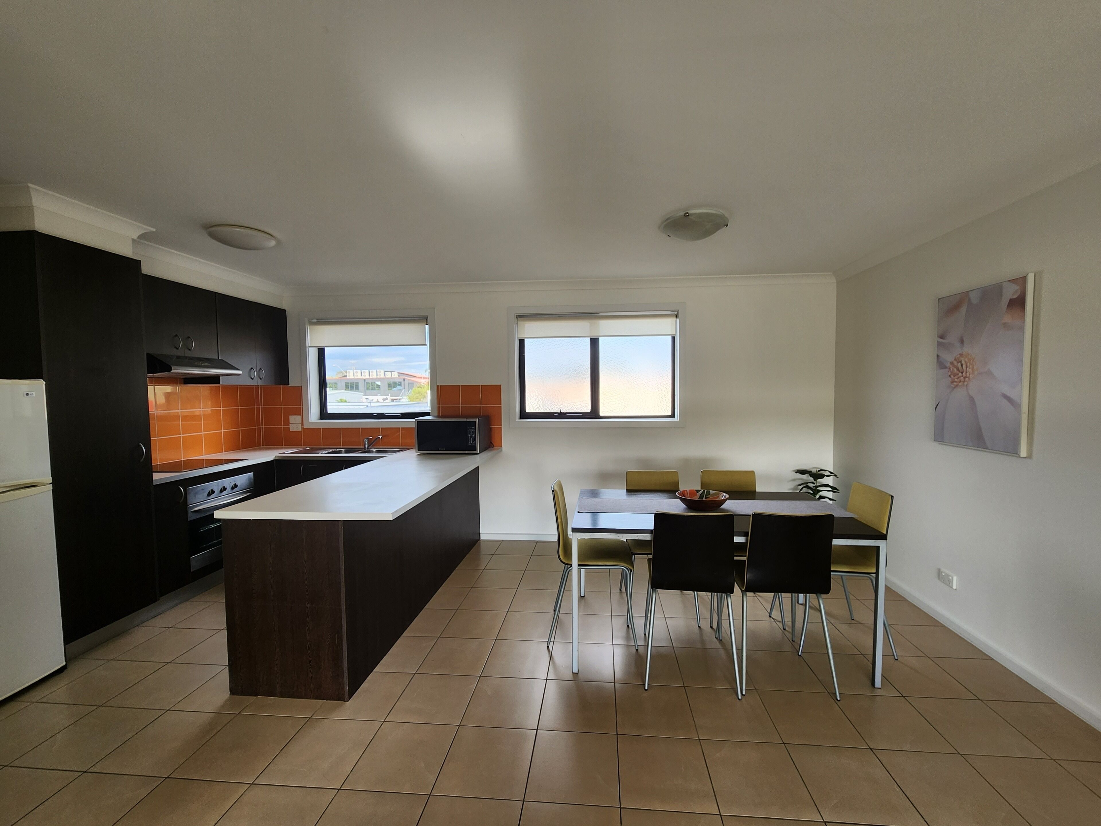 Una cocina moderna con una isla central, armarios negros y un comedor con mesa y sillas.