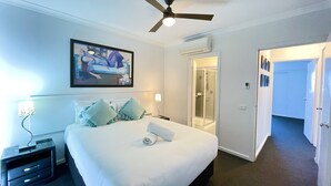 A hotel room with a bed, a ceiling fan, a shower, and a door leading to another room. - Oceanic On Thompson Apartments (Cowes)