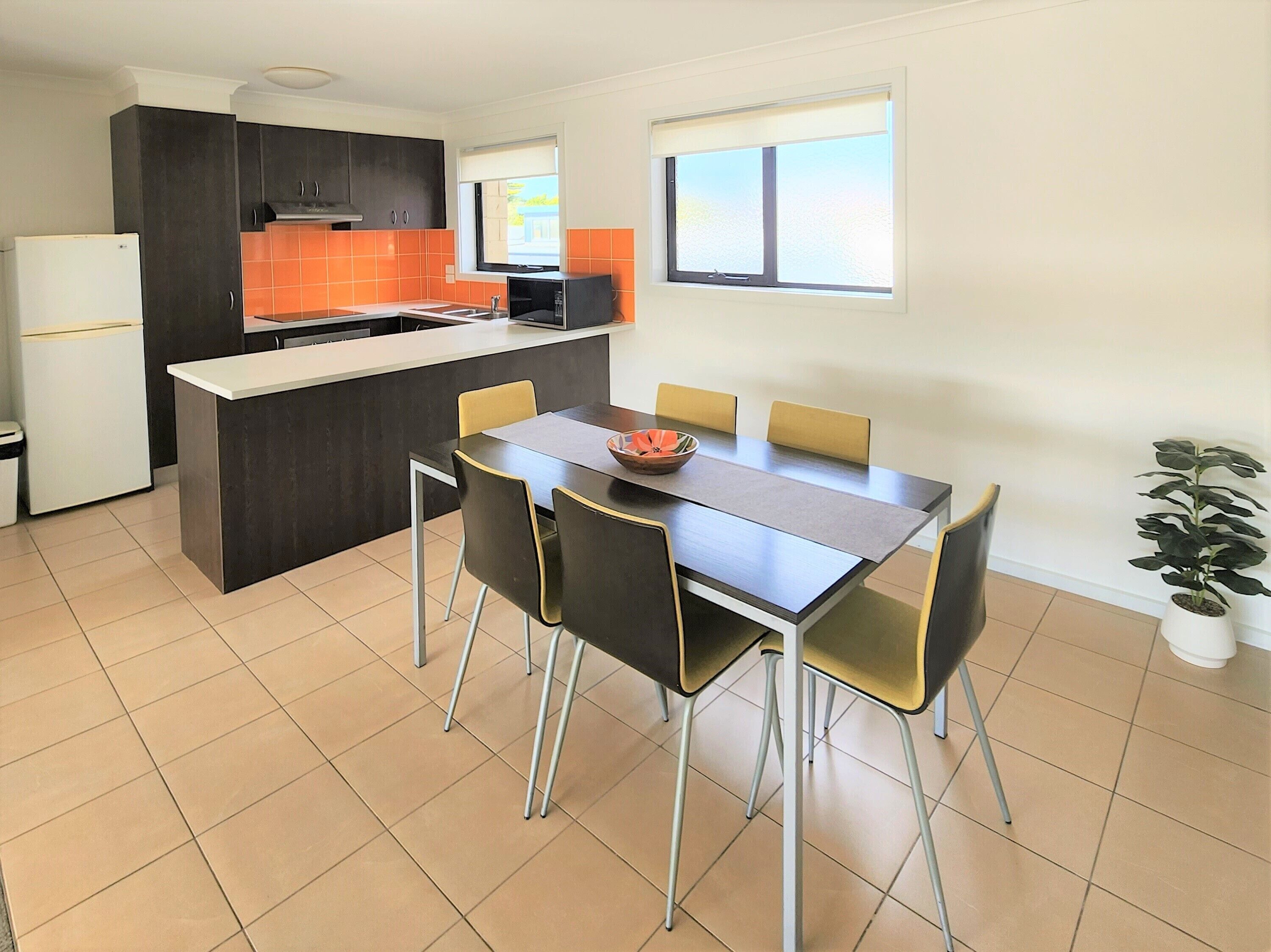 Een moderne keuken met een centraal eiland, een eettafel met stoelen en een potplant.