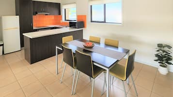 Een moderne keuken met een centraal eiland, een eettafel met stoelen en een potplant.