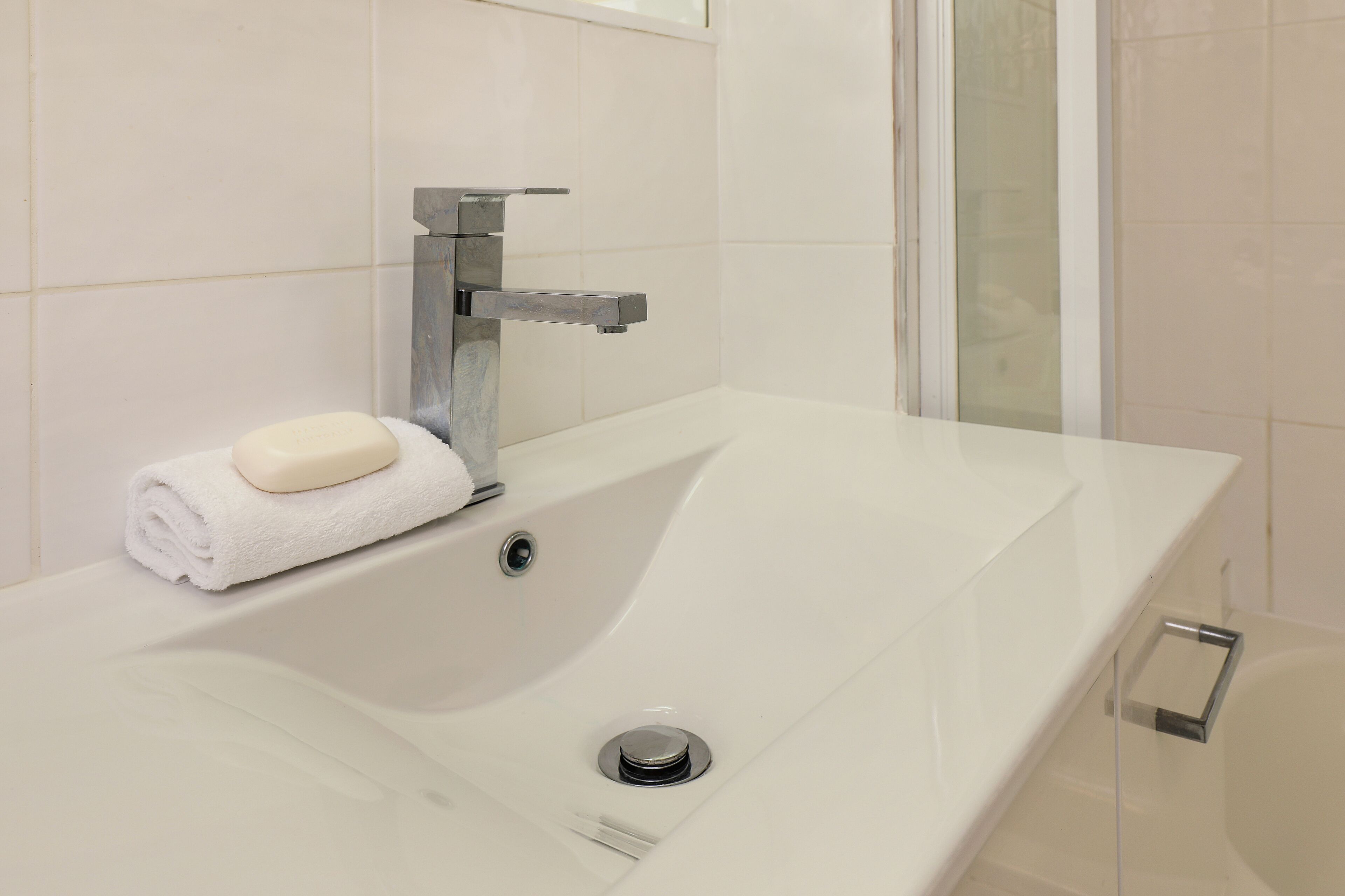 A modern bathroom with a white sink, a towel, and a soap bar.