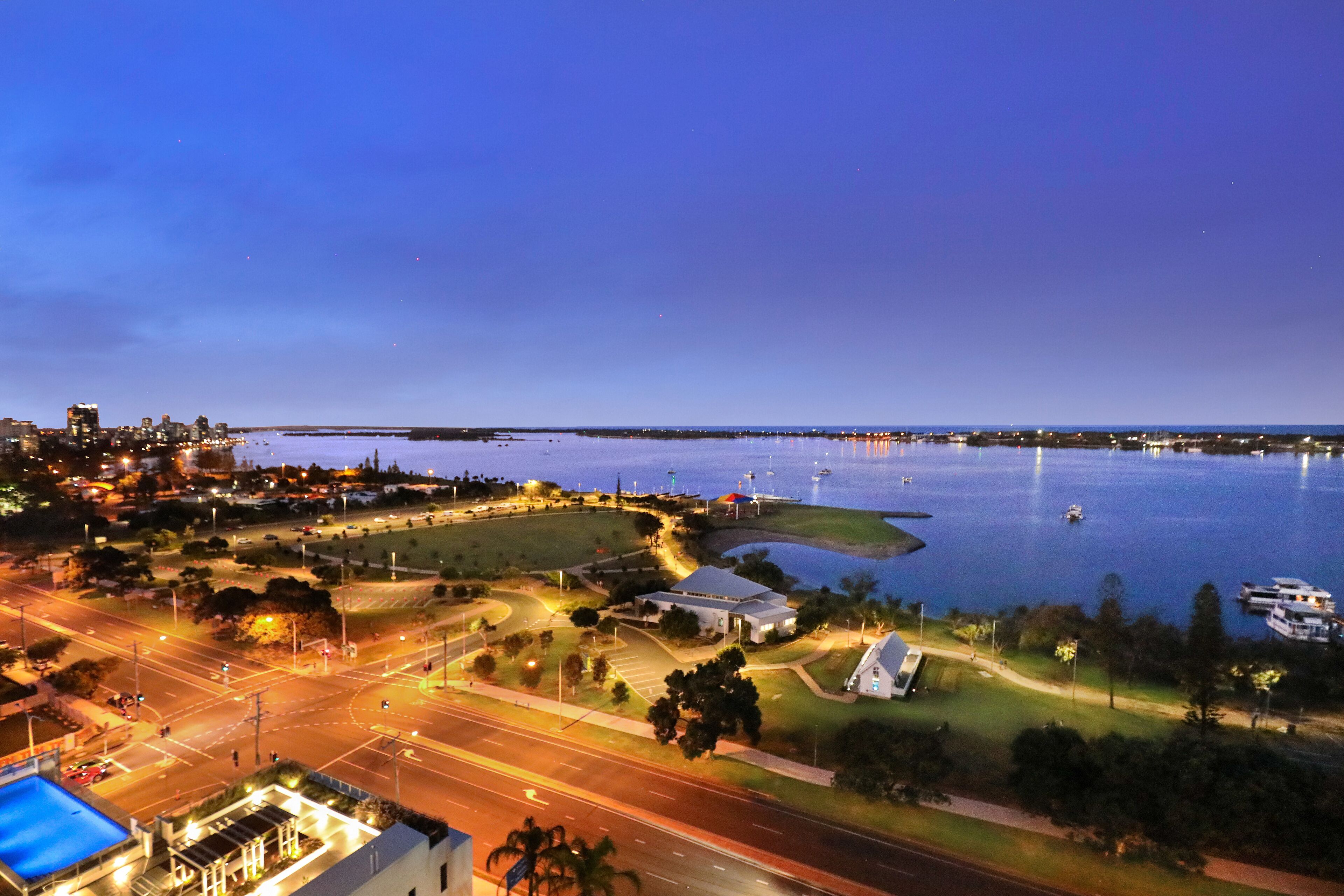 An aerial view of a coastal city at dusk with a marina, roads, and buildings.