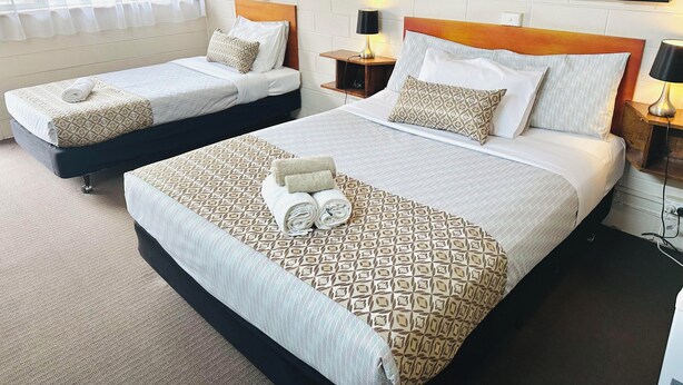 Habitació d'hotel amb dos llits, cadascun amb capçalera de fusta, roba de llit blanca i coixins estampats. Hi ha taules de nit amb làmpades i una finestra amb cortines translúcides.