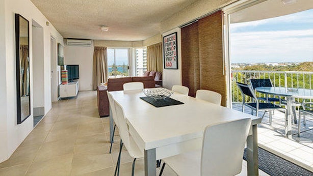 A spacious room with a balcony, a dining area, and a large window offering a view.