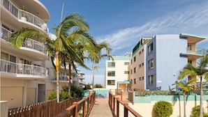 A pathway leading to a building with balconies and a pool area.