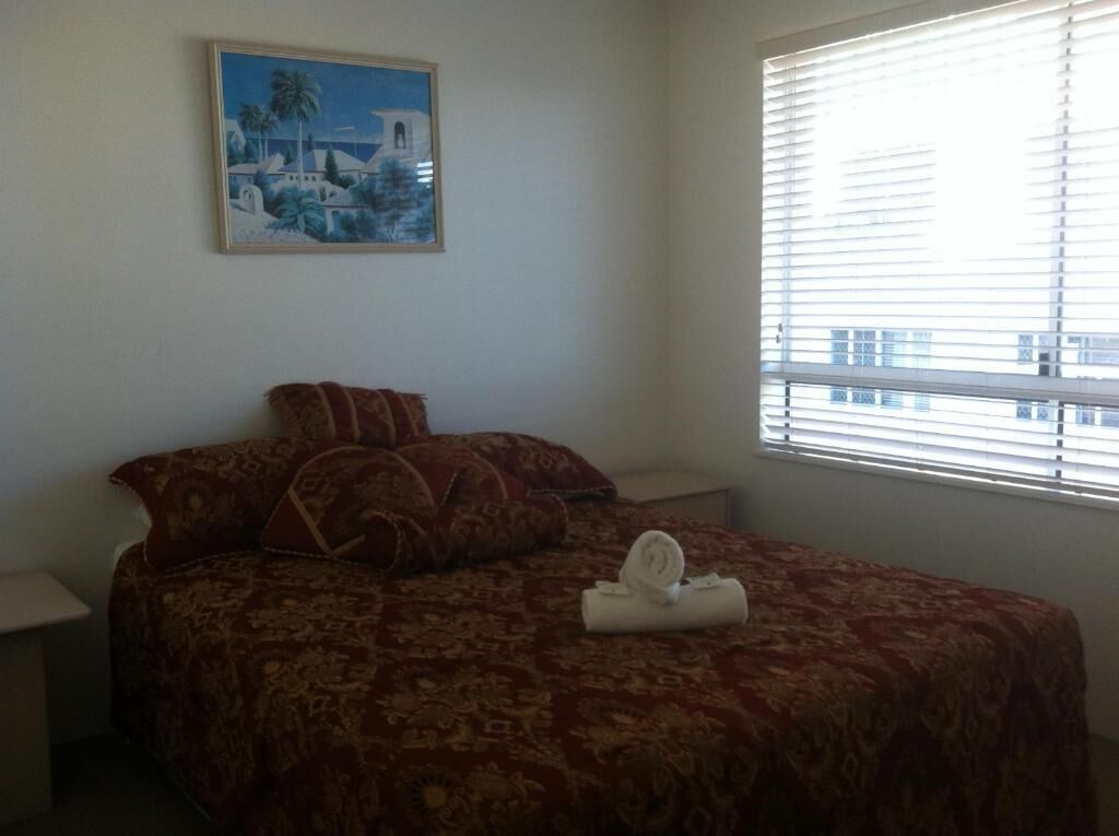Un dormitorio con cama, almohadas, un cuadro y una ventana con persianas.