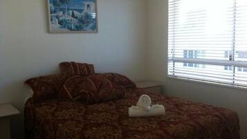 Un dormitorio con cama, almohadas, un cuadro y una ventana con persianas.