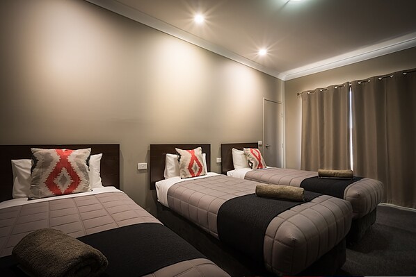 A hotel room with three beds, each with a headboard, a large mirror, and a window with curtains.