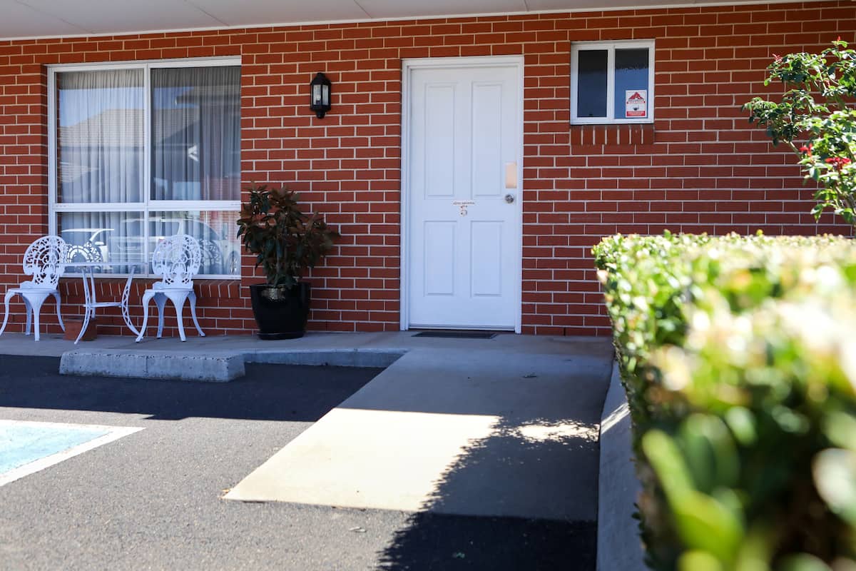 A red brick building with a white door, a small window, and outdoor seating with white chairs.