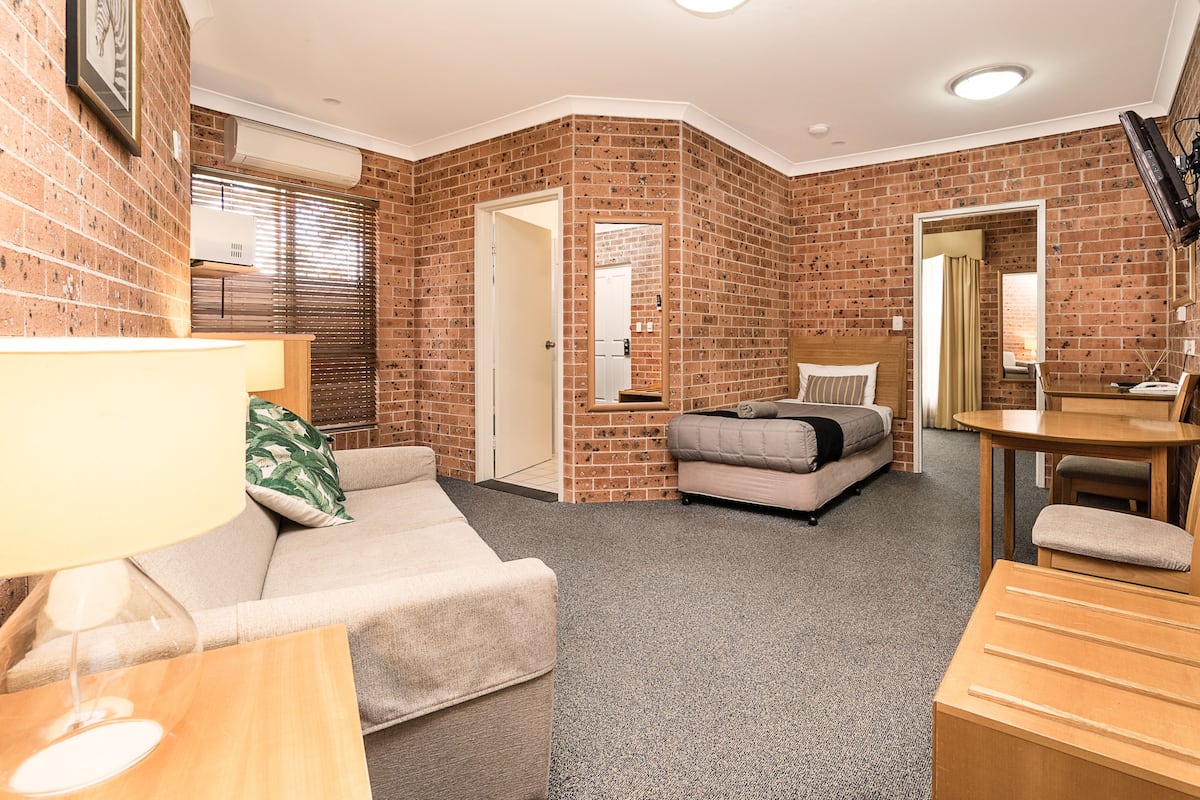 A compact room with a brick wall, a sofa, a bed, a small table, and a TV.