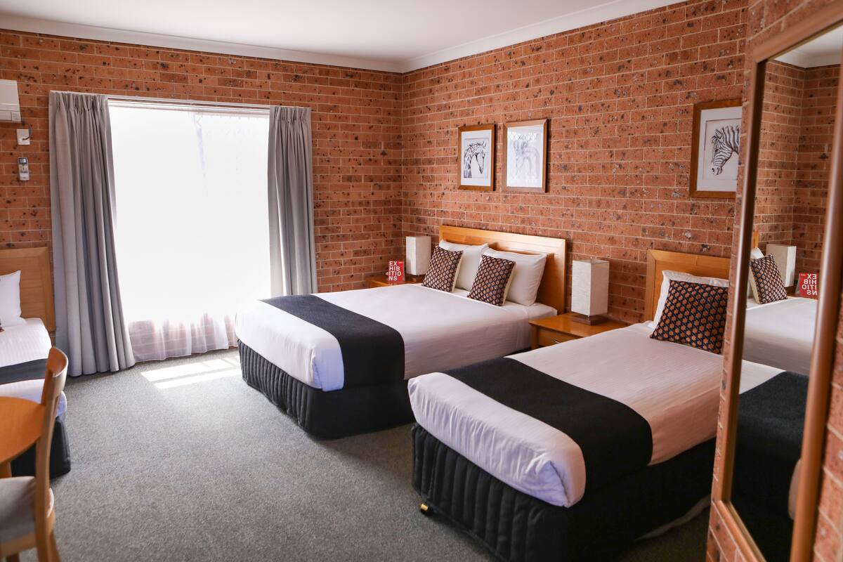 A hotel room with two beds, a brick wall, and a large window with curtains.
