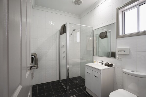 A modern bathroom with a glass shower enclosure, white tiles, a white sink with a mirror, and a toilet.