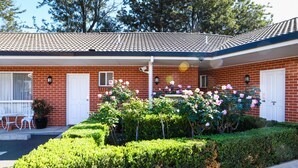 A two-story brick building with a tiled roof, a covered porch, and a well-maintained garden with roses. - Akuna Motor Inn and Apartments (Dubbo)