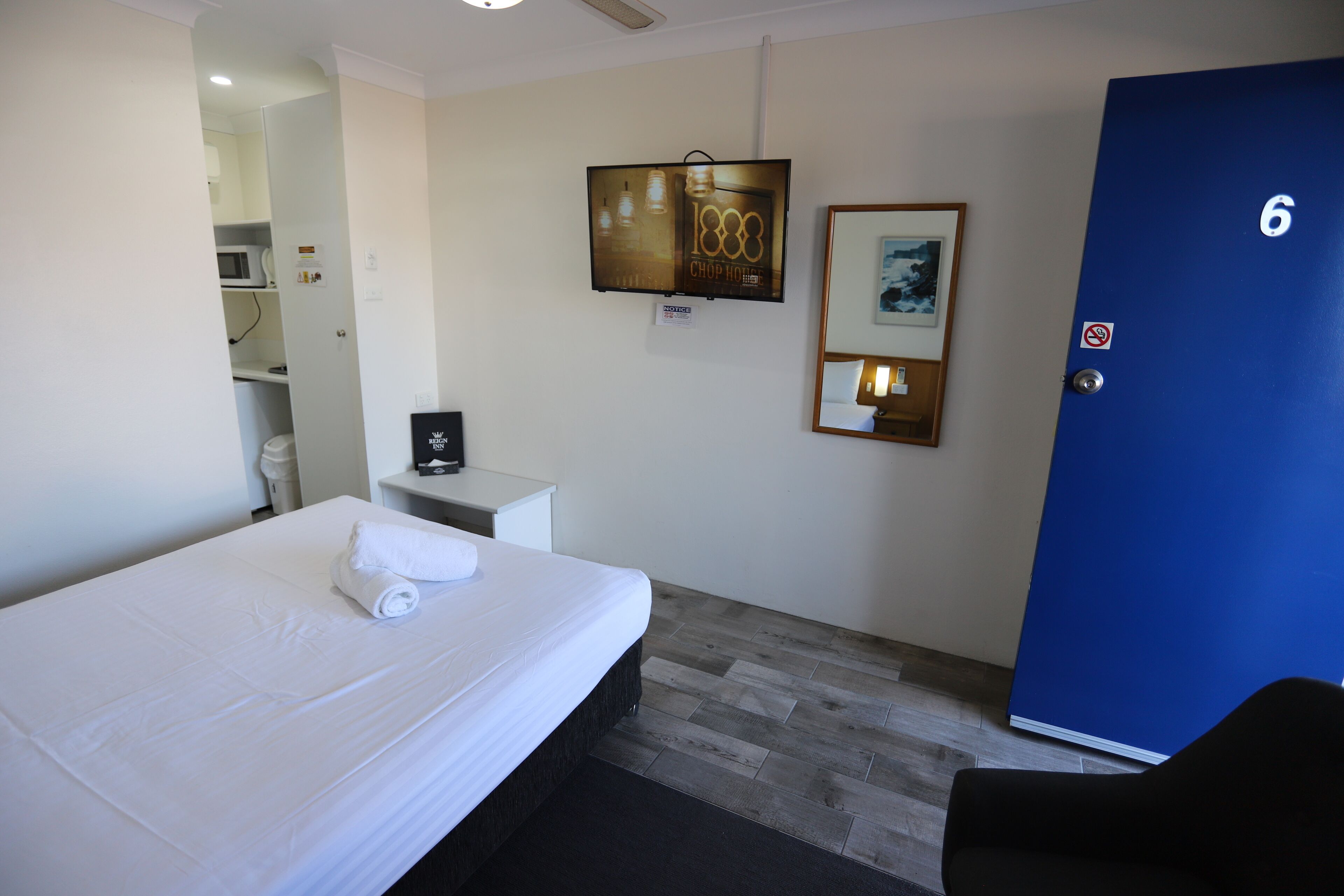 Habitació d'hotel amb llit, escriptori, porta blava i televisió penjada a la paret.