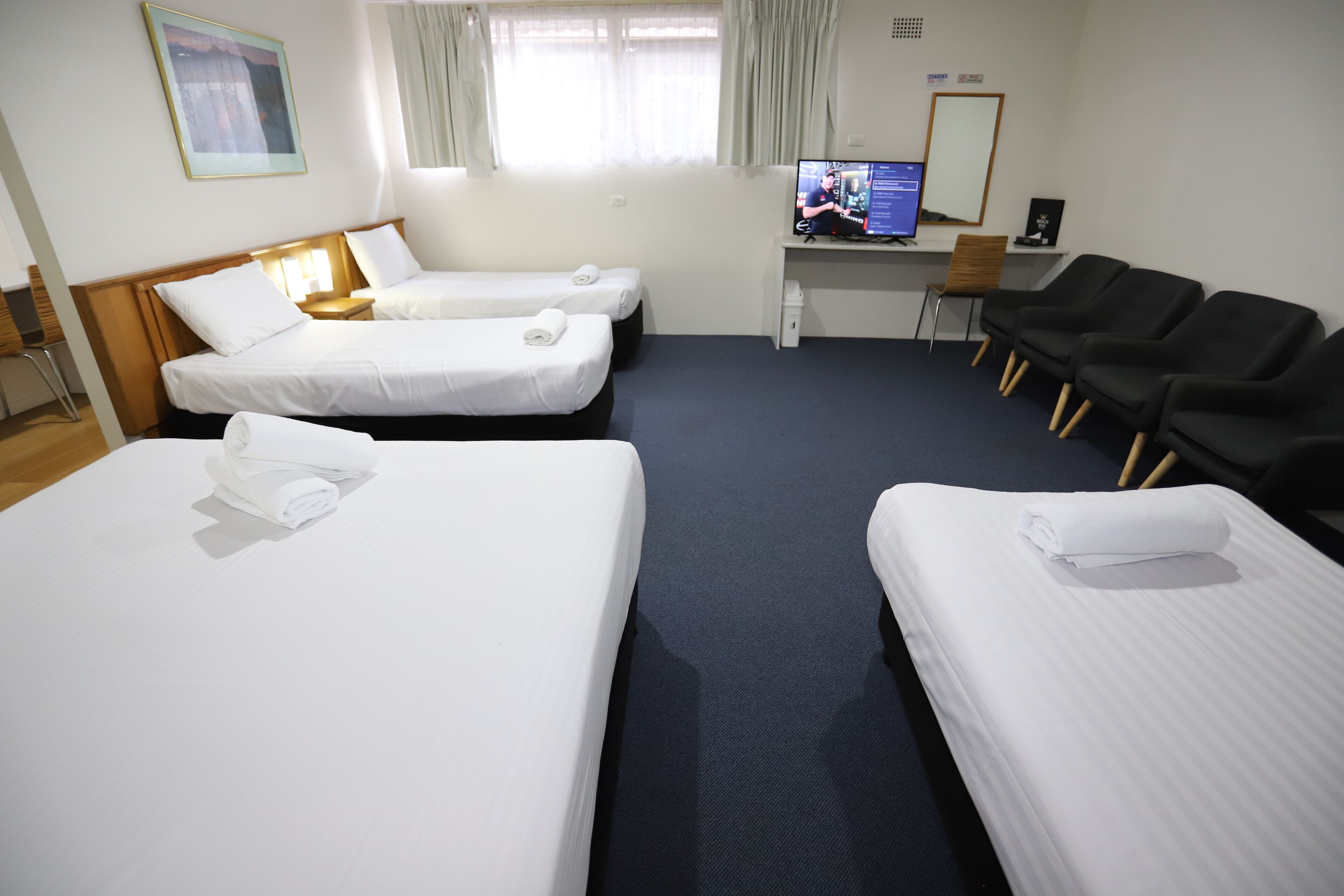Habitación de hotel con dos camas individuales, un escritorio con computadora y una zona de estar con sillas.