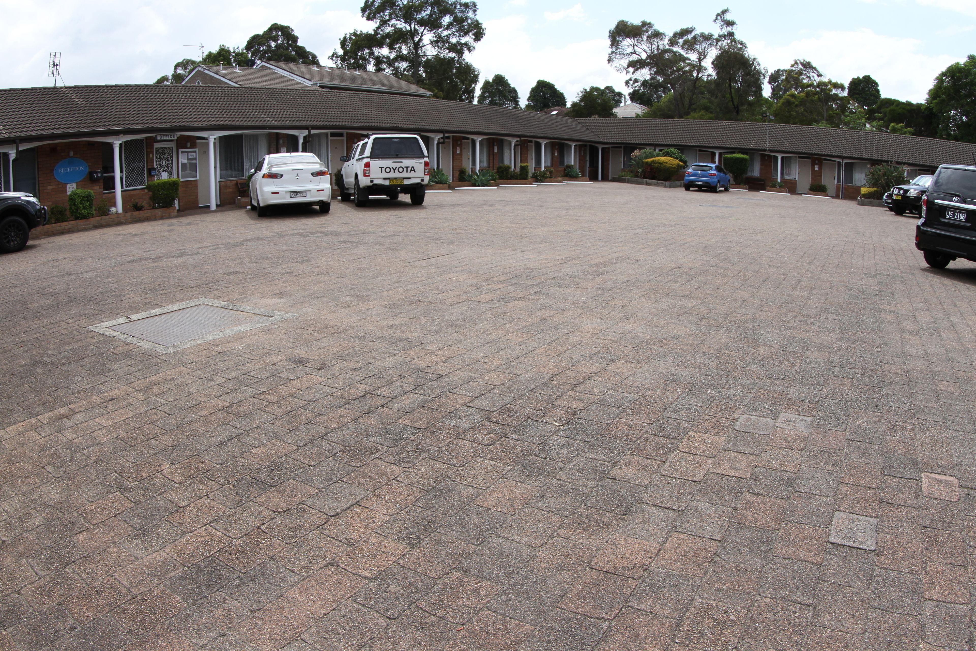 A motel with a paved driveway, several parked cars, and a row of rooms with a consistent architectural style.