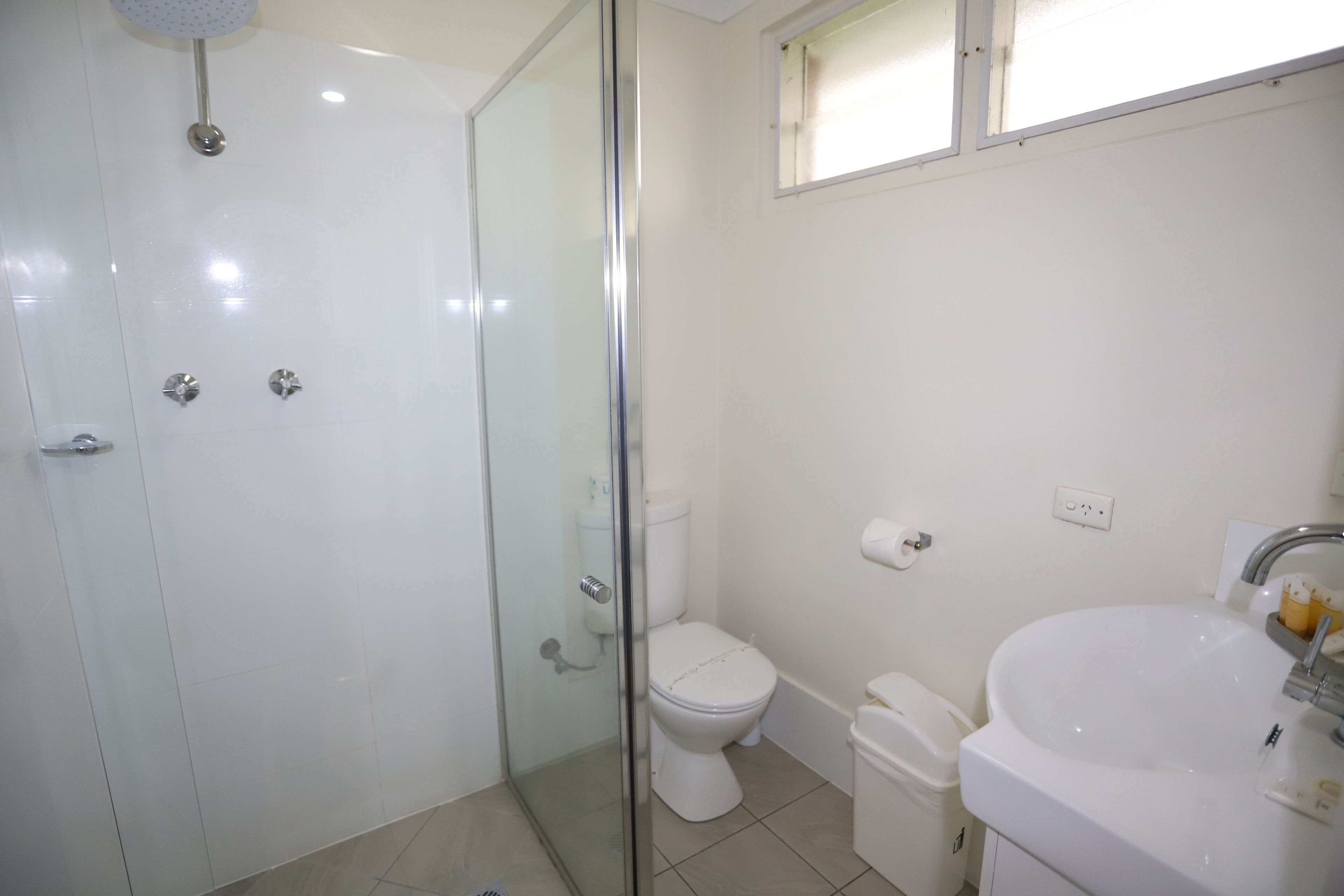 A bathroom with a glass-enclosed shower, a toilet, and a sink.