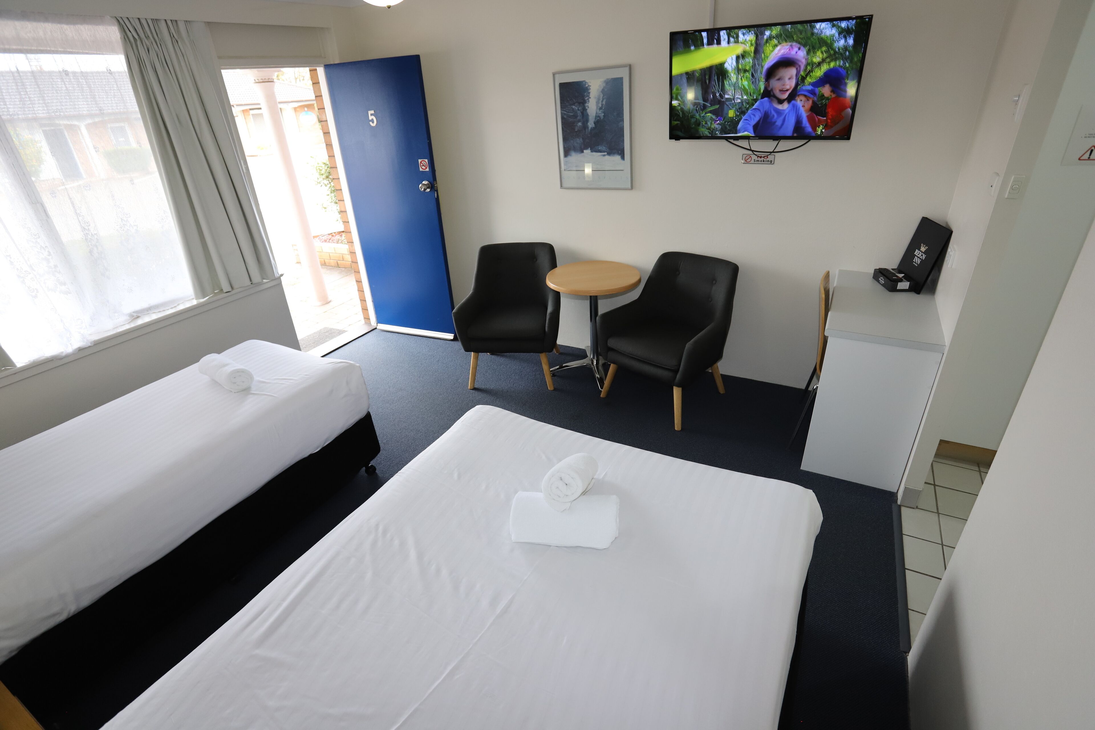 Une chambre d’hôtel avec deux lits, une petite table, deux chaises, un téléviseur et une porte portant le numéro 5.