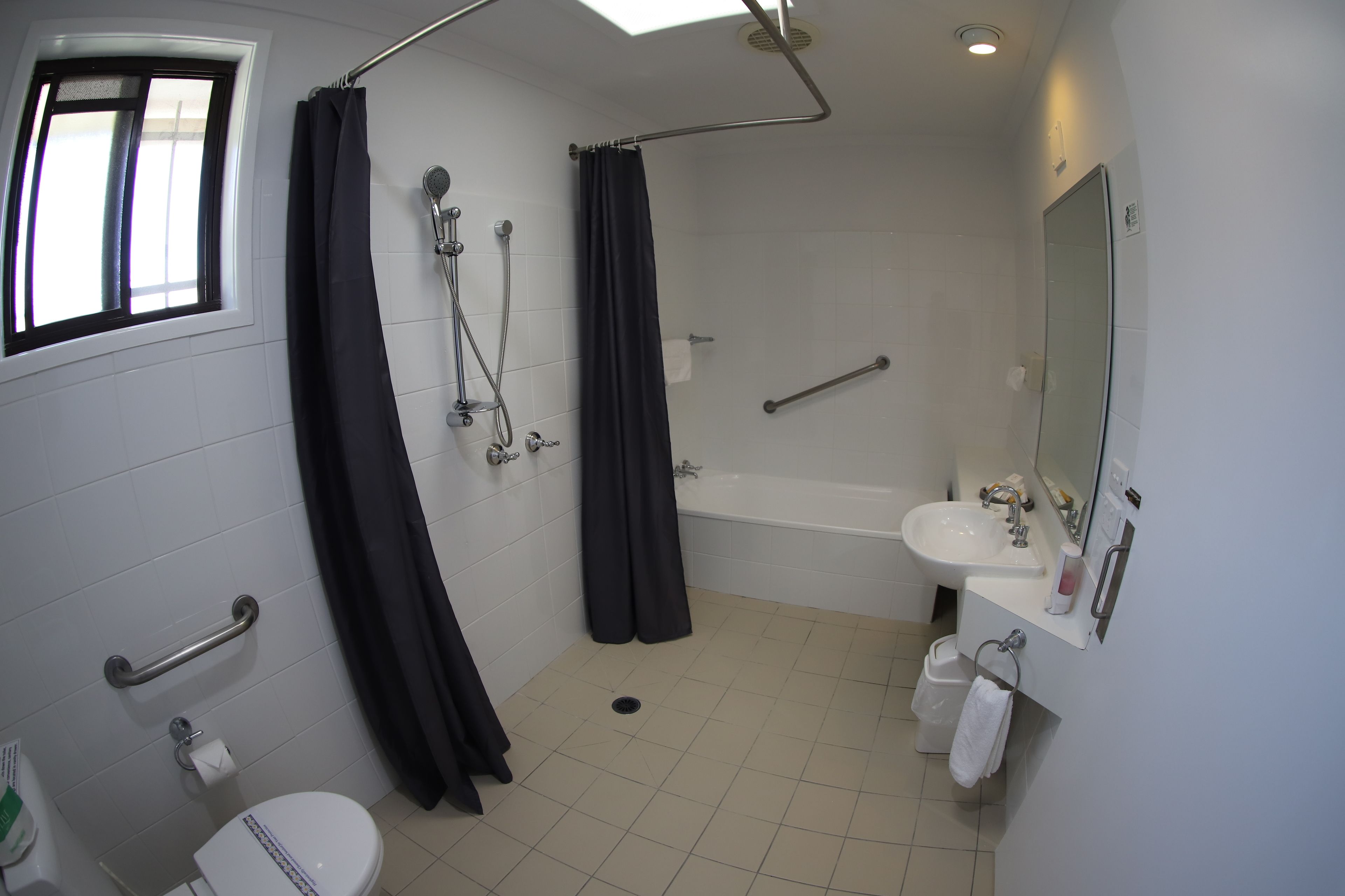 A bathroom with a toilet, sink, shower, and a window.