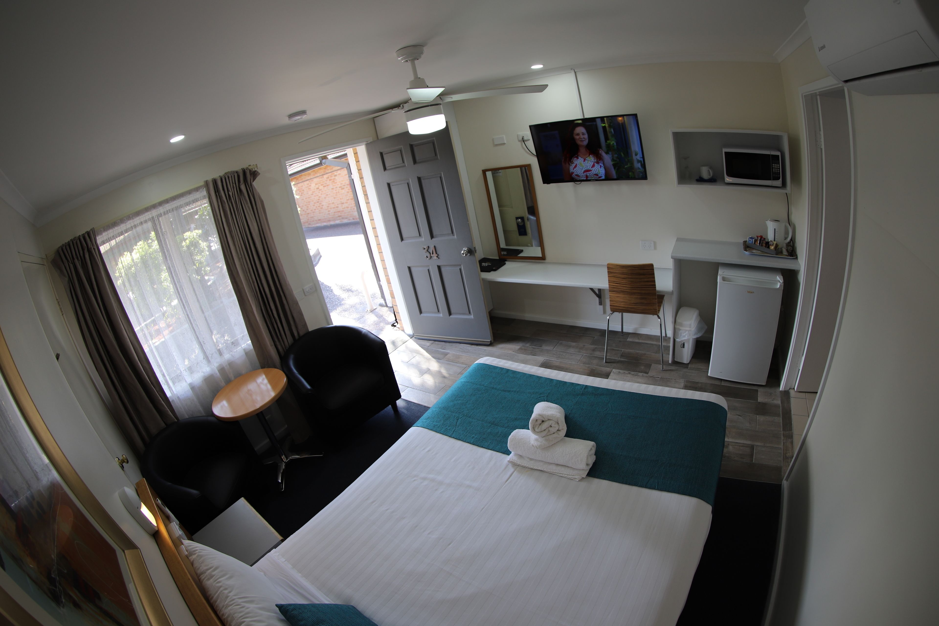 Una habitación de hotel con cama, escritorio, silla, televisión y microondas.