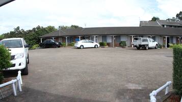 A motel with a paved driveway, a white car, a black car, and a white truck parked in front.