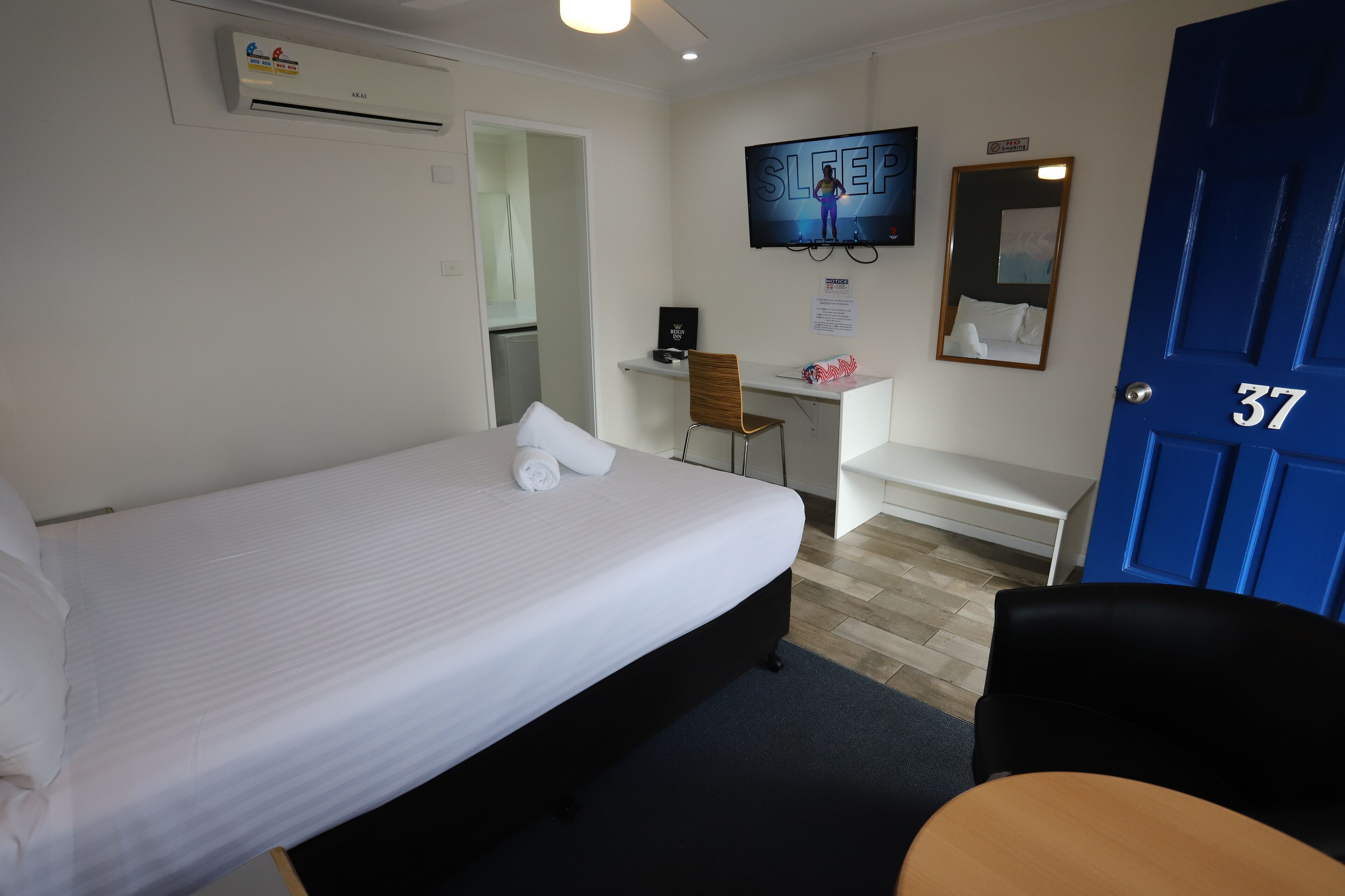 Quarto de hotel com uma cama, uma mesa, uma cadeira, uma TV e uma porta azul com o número 37.