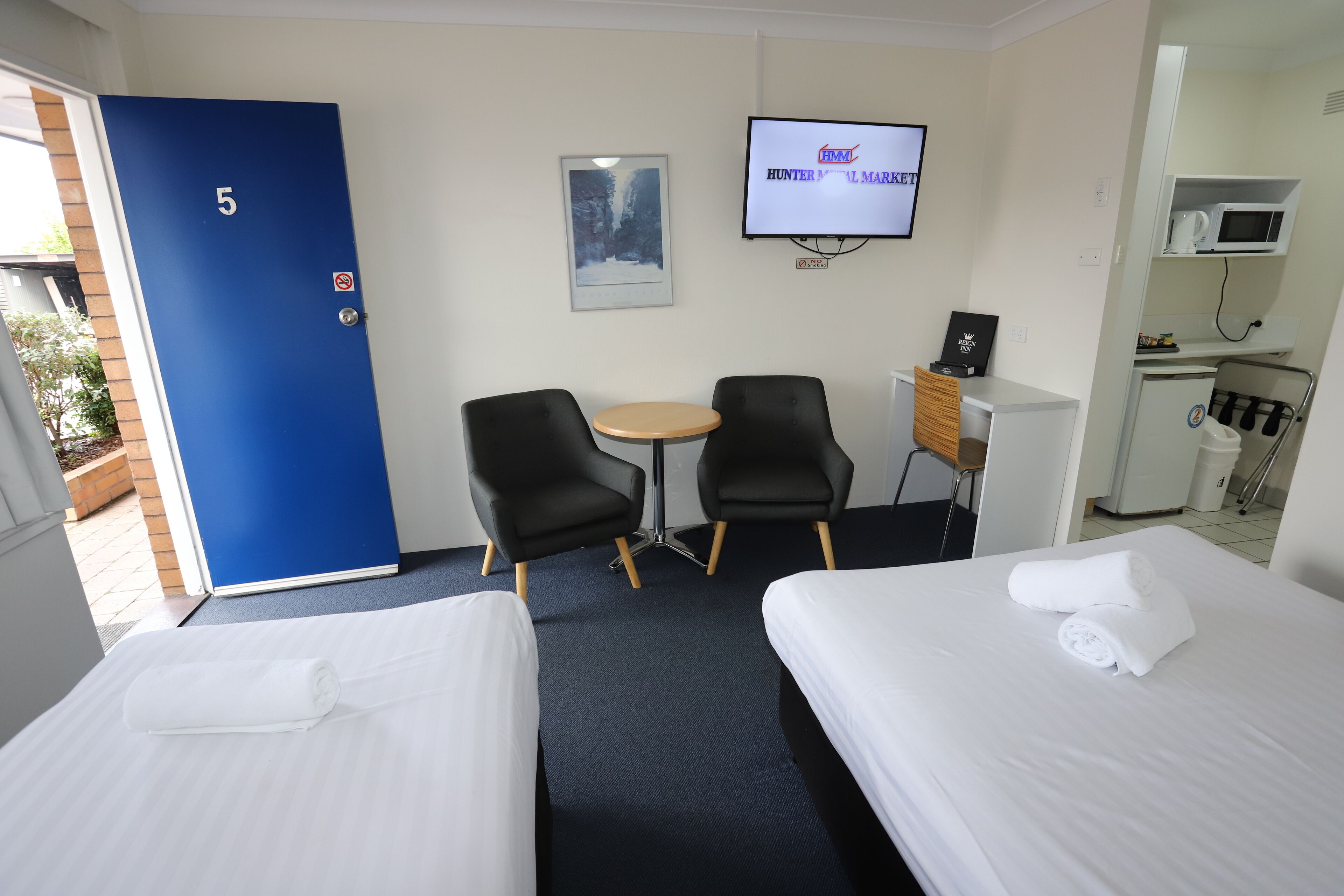Une chambre d’hôtel avec deux lits, un bureau, deux chaises, une télévision et un four à micro-ondes.