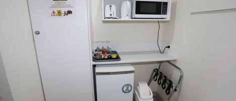 A compact kitchenette with a microwave, toaster, and small fridge. A trash bin and a shoe rack are also visible.