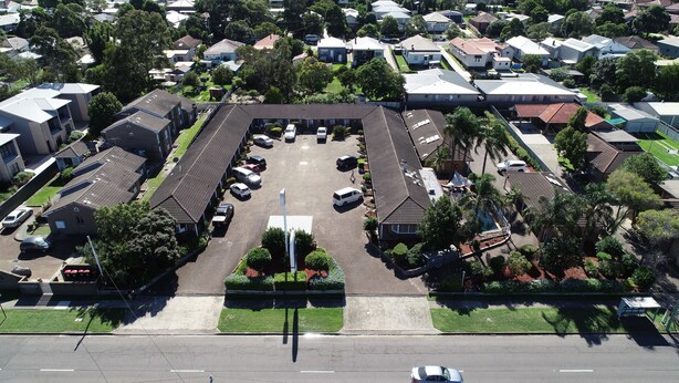 An aerial view of a residential area with a large parking lot, multiple houses, and a central building with a flat roof.