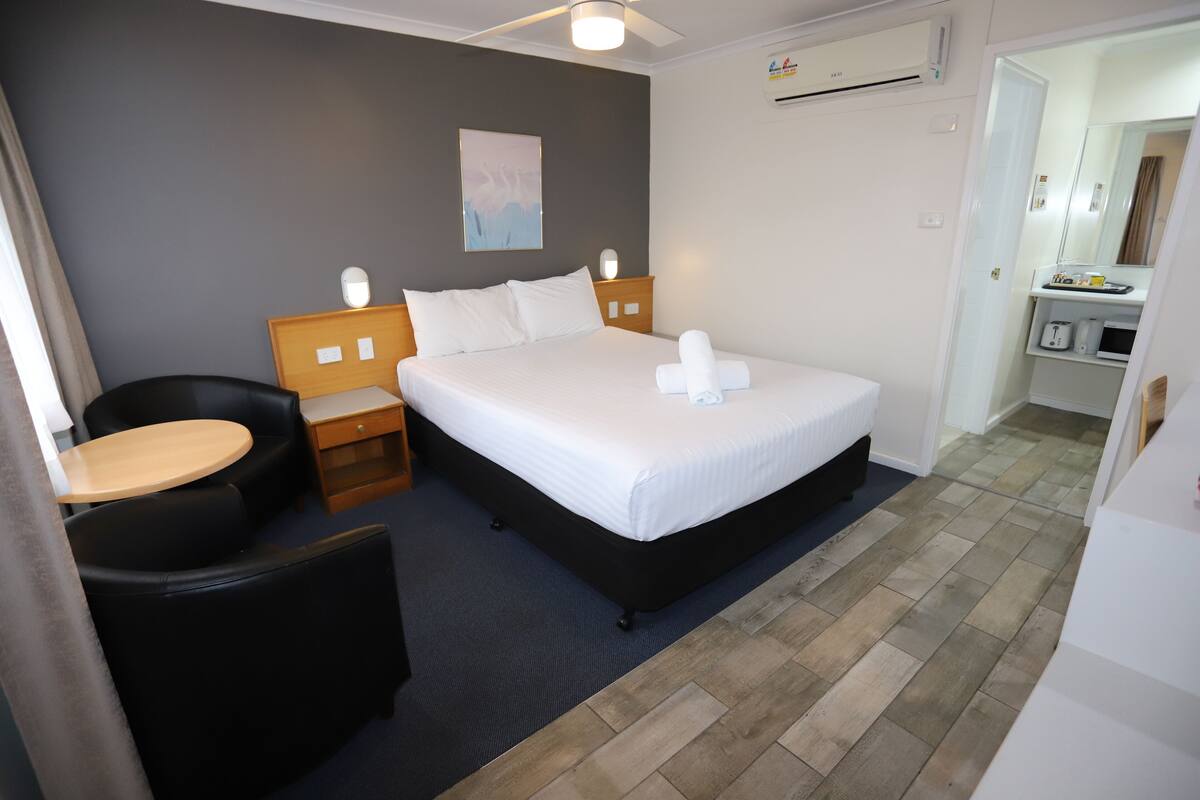 A hotel room with a bed, a desk, a chair, and a small table.