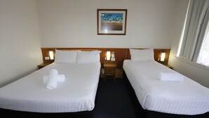 A hotel room with two beds, each with white linens and a rolled towel. There is a framed picture on the wall above the beds.