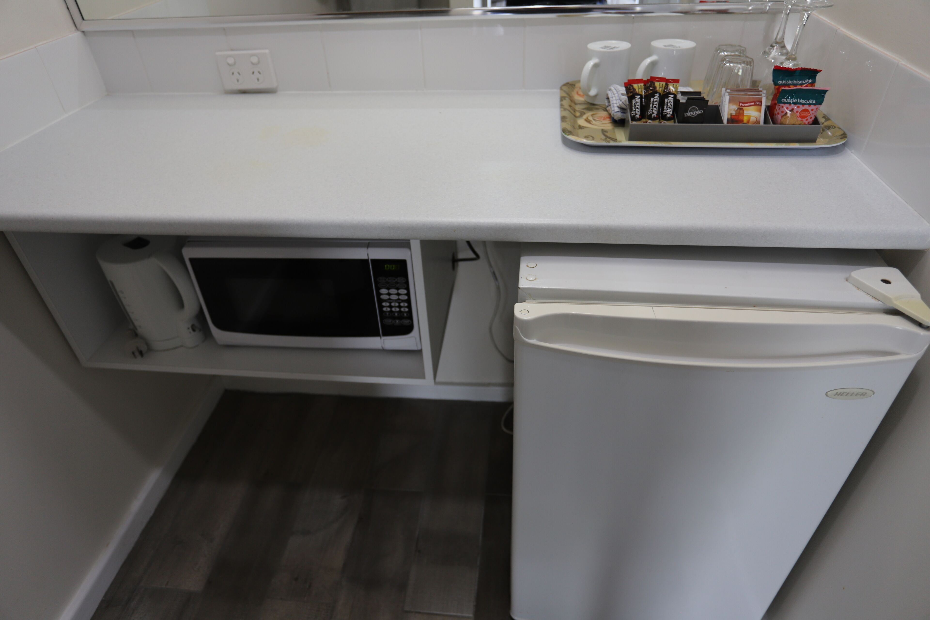 A compact kitchenette with a microwave, refrigerator, and a tray of snacks.