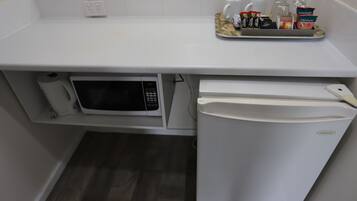 A compact kitchenette with a microwave, refrigerator, and a tray of snacks.