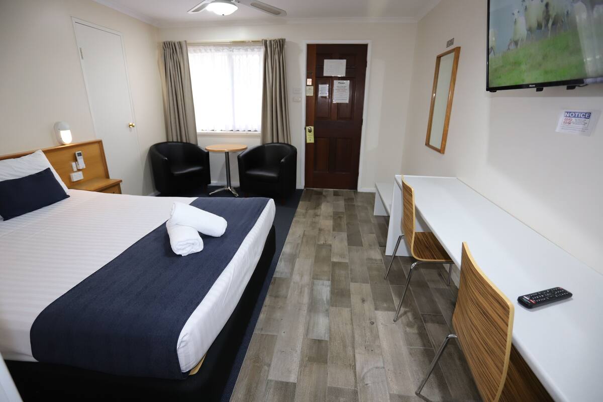 A hotel room with a bed, two chairs, a small table, a desk, and a TV.