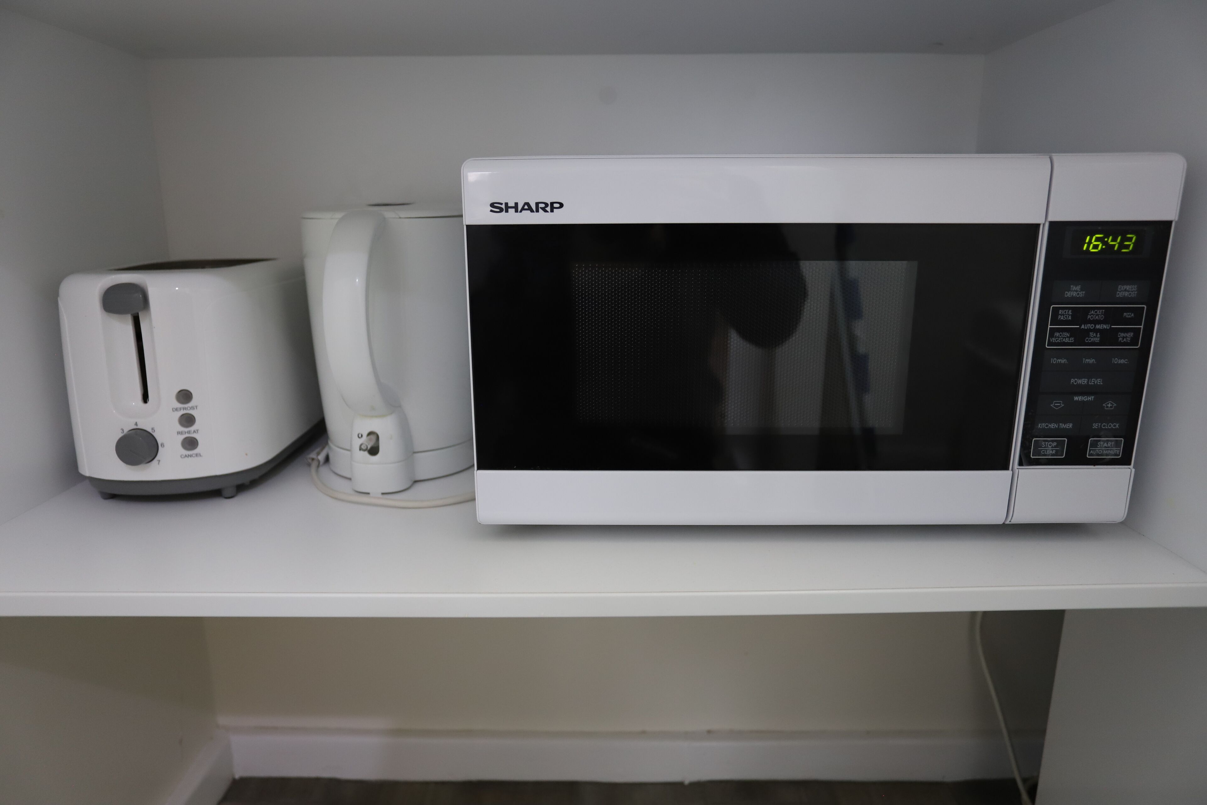 A microwave and toaster on a white shelf.