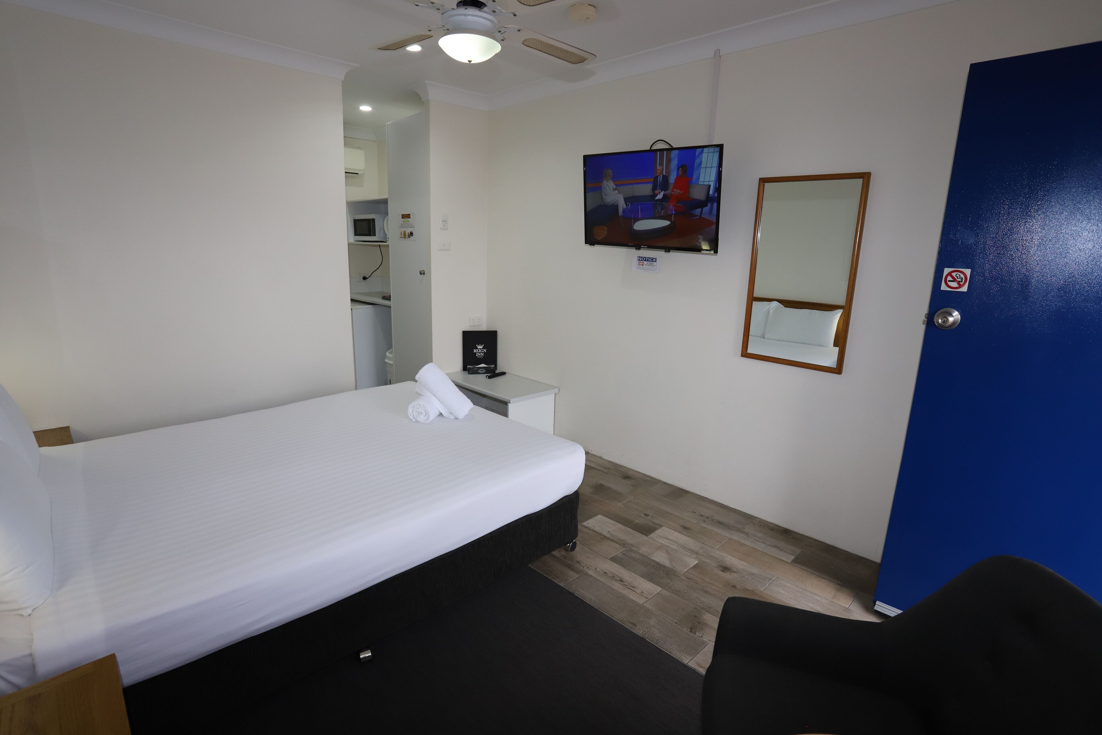 Una camera d'albergo con un letto singolo, una piccola scrivania con una sedia, un televisore fissato alla parete e una porta blu.