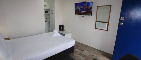 Una camera d'albergo con un letto singolo, una piccola scrivania con una sedia, un televisore fissato alla parete e una porta blu.